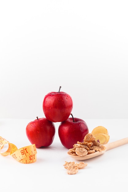 Tres manzanas con cinta métrica y cereales en cuchara.