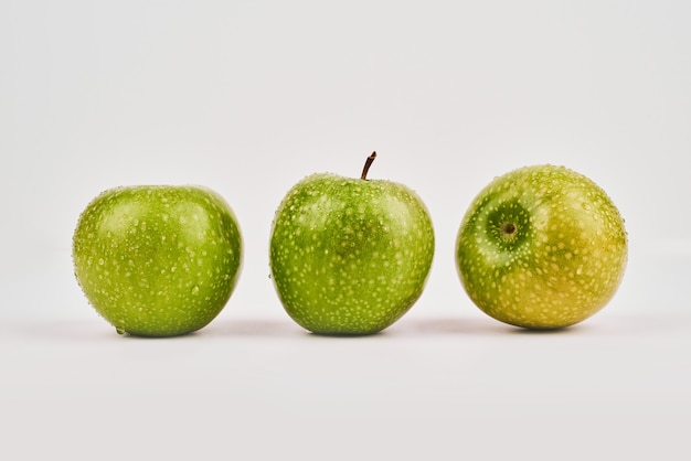 Tres manzanas enteras sobre superficie blanca.