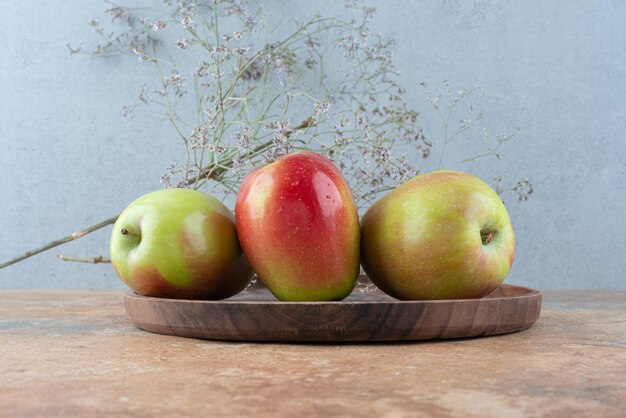 Tres manzanas frescas con flor marchita sobre placa de madera