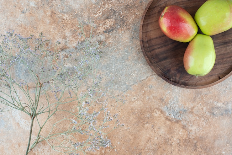 Foto gratuito tres manzanas frescas con flor marchita sobre plancha de madera.