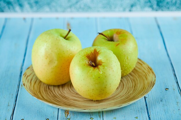 Tres manzanas jugosas en plato de cerámica y mesa azul.