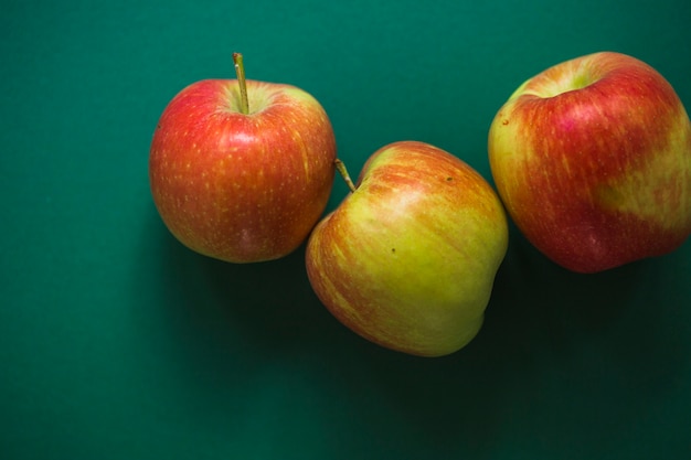 Tres manzanas rojas enteras sobre fondo verde