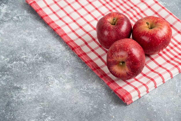 Tres manzanas rojas con mantel a rayas sobre superficie de mármol.