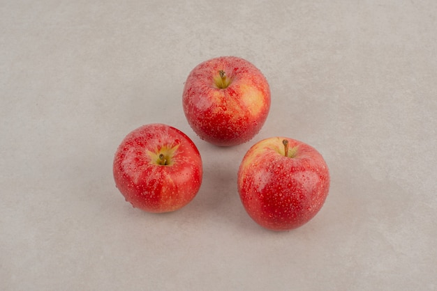 Tres manzanas rojas sobre la mesa de mármol.