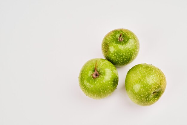 Tres manzanas verdes sobre superficie blanca.