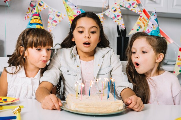 Tres muchachas bonitas que soplan velas en la torta en la fiesta de cumpleaños