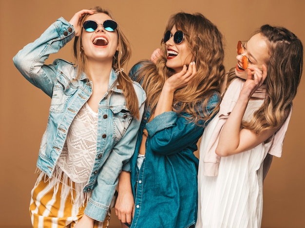 Tres muchachas sonrientes hermosas jovenes en ropa casual de los vaqueros del verano moderno. Sexy mujer despreocupada posando. Modelos positivos en gafas de sol