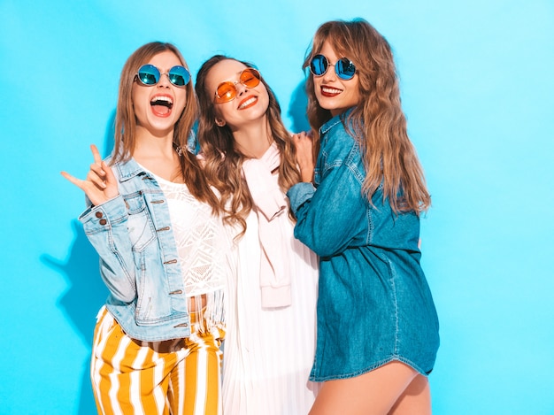 Tres muchachas sonrientes hermosas jovenes en ropa casual de los vaqueros del verano moderno. Sexy mujer despreocupada posando. Modelos positivos en gafas de sol