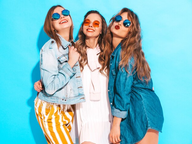 Tres muchachas sonrientes hermosas jovenes en ropa casual de los vaqueros del verano moderno. Sexy mujer despreocupada posando. Modelos positivos en gafas de sol