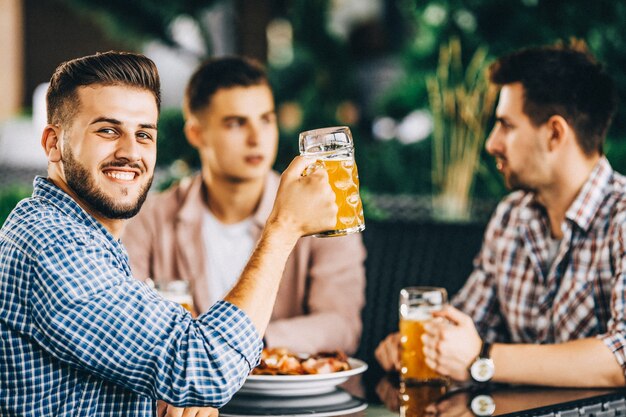 Tres muchachos reunidos en el bar, están comiendo y bebiendo cerveza