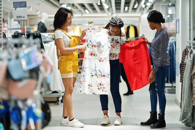 Tres mujeres africanas eligiendo ropa en la tienda Día de compras