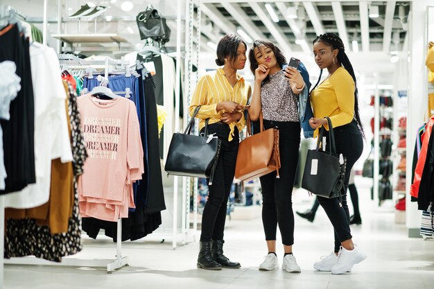 Tres mujeres africanas en la tienda de ropa con bolsos nuevos Día de compras Miran los teléfonos móviles