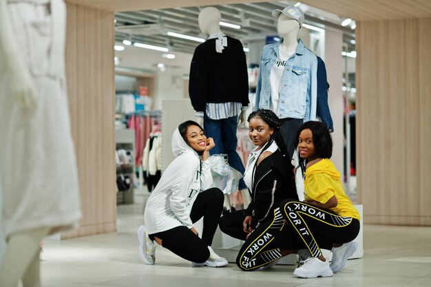 Tres mujeres afroamericanas en chándales de compras en el centro comercial de ropa deportiva contra el tema de la tienda deportiva maniquí