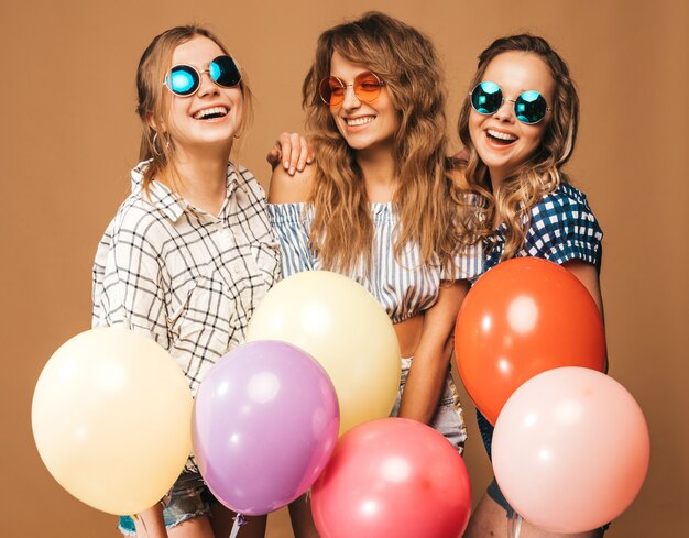 Tres mujeres hermosas sonrientes en ropa de verano camisa a cuadros. Chicas posando Modelos con globos de colores en gafas de sol. Divirtiéndose, listo para celebrar cumpleaños