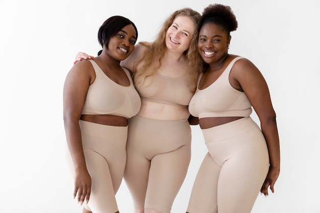 Foto gratuita tres mujeres sonrientes seguras posando mientras usa un modelador de cuerpo