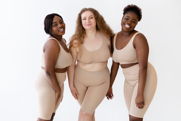 Foto gratuita tres mujeres sonrientes seguras posando mientras usa un modelador de cuerpo