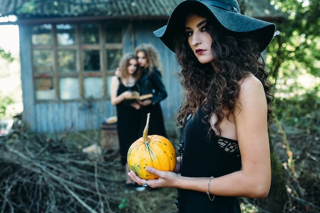 Tres mujeres vintage como brujas, posan frente a un edificio abandonado en la víspera de Halloween