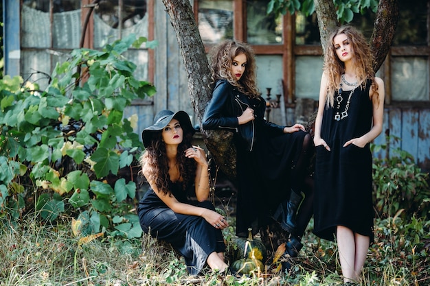 Tres mujeres vintage como brujas, posan frente a un edificio abandonado en la víspera de Halloween