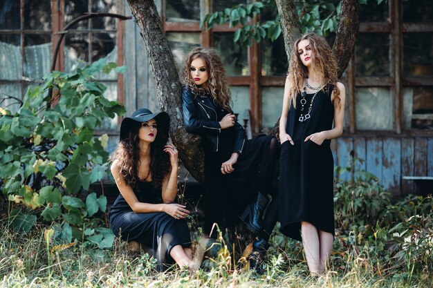 Tres mujeres vintage como brujas, posan frente a un edificio abandonado en la víspera de Halloween