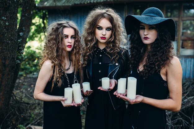 Tres mujeres vintage como brujas, posan y sostienen en sus manos las velas en la víspera de Halloween