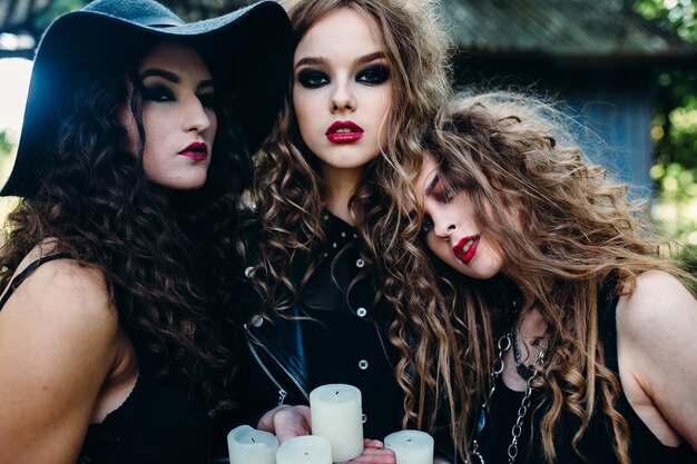 Tres mujeres vintage como brujas, posan y sostienen en sus manos las velas en la víspera de Halloween