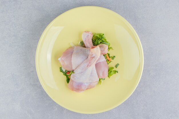 Tres muslos de pollo y verde, en el plato, sobre la superficie blanca