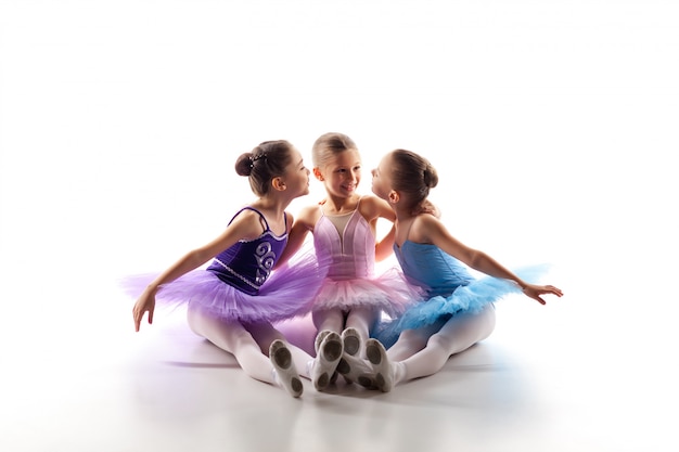 Foto gratuita tres niñas de ballet sentado en tutú y posando juntos
