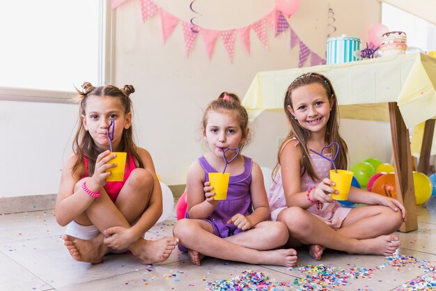 Tres niñas beben jugo mientras celebran la fiesta de cumpleaños en casa