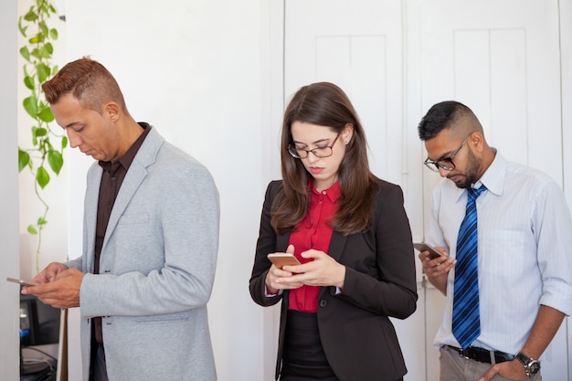 Tres oficinistas enfocados en smartphones.