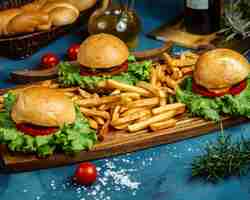 Foto gratuita tres pequeñas hamburguesas de carne y papas fritas servidas sobre tabla de madera