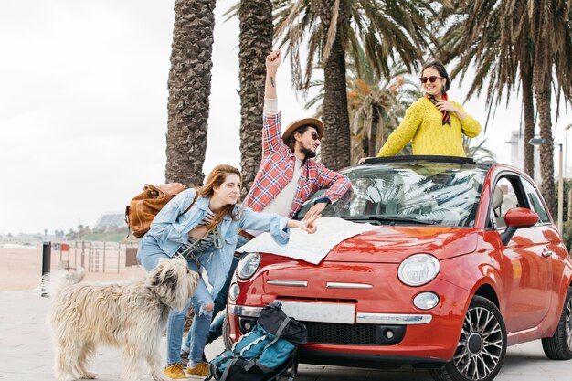 Tres personas y un perro de pie cerca de un coche con un mapa de carreteras