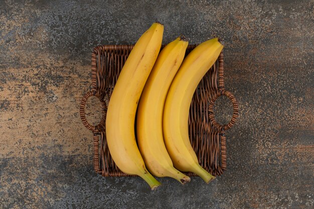 Foto gratuita tres plátanos maduros en canasta de madera