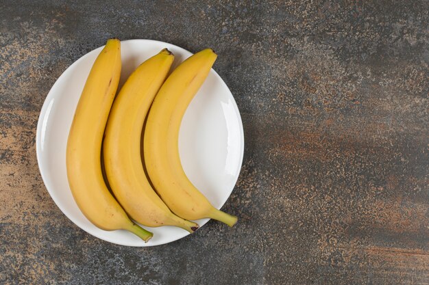 Tres plátanos maduros en un plato blanco.