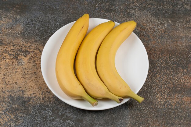 Tres plátanos maduros en un plato blanco.