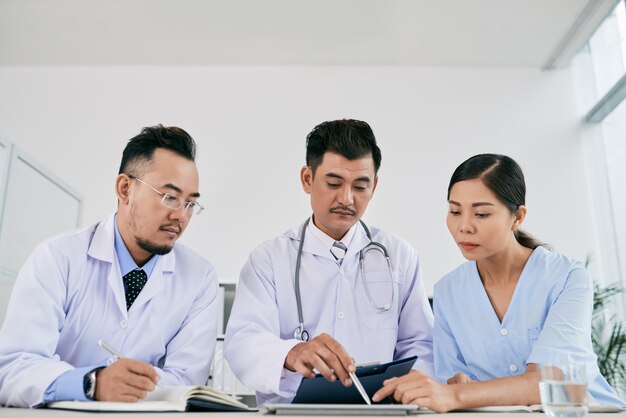 Tres profesionales médicos masculinos y femeninos que discuten el historial médico del paciente