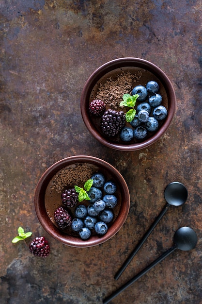 Foto gratuita tres ramekins con mousse de chocolate con arándanos moras y menta fresca en un fondo de hierro oxidado vertical