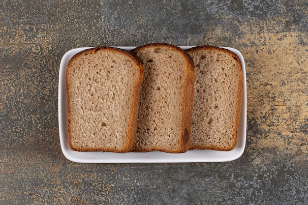 Tres rebanadas de pan negro en un plato cuadrado blanco.