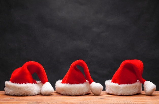 Foto gratuita los tres sombreros rojos de santa en la mesa de madera sobre fondo negro