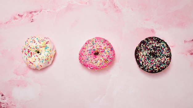 Foto gratuita tres tipos de blanco; rosquillas rosadas y chocolate con chispas contra fondo rosa