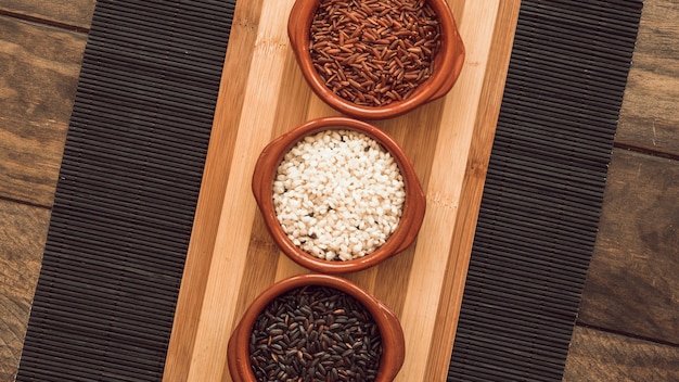 Tres tipos diferentes de cuencos de granos de arroz en mantel sobre la mesa de madera