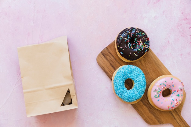 Foto gratuita tres tipos diferentes de donuts cerca del paquete sobre fondo rosa