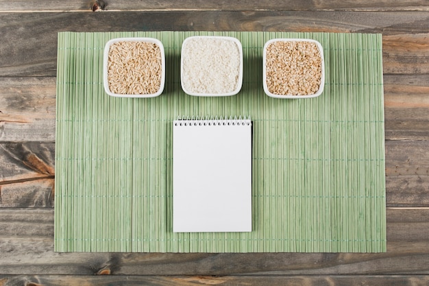 Tres tipos diferentes de tazones de arroz crudo con bloc de notas en espiral sobre mantel verde sobre la mesa