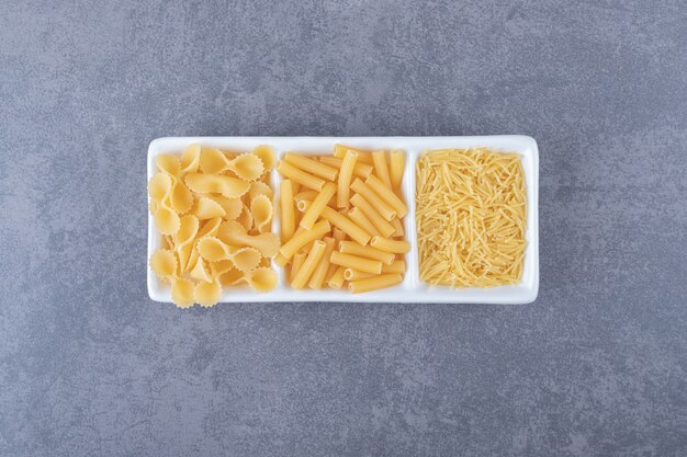 Tres tipos de pasta cruda en un plato blanco.