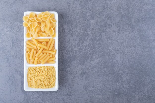 Tres tipos de pasta cruda en un plato blanco.