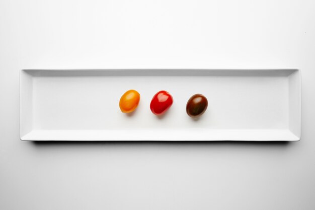 Tres tomates cherry diferentes aislados en el centro del plato blanco, vista superior, amarillo, rojo y negro