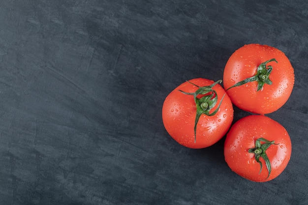 Tres tomates frescos enteros sobre un fondo oscuro.