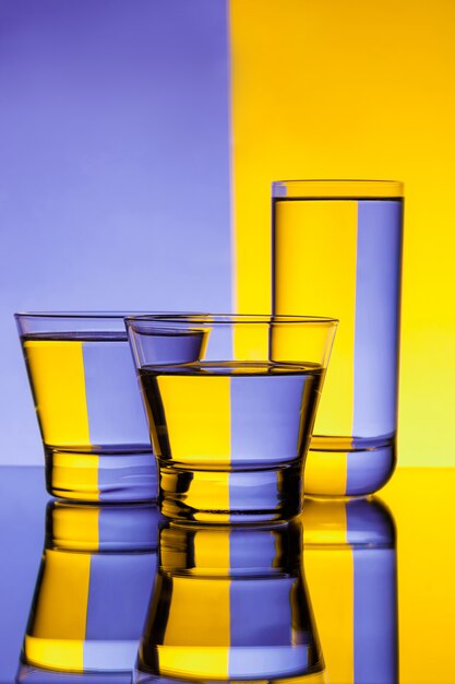 Tres vasos con agua sobre fondo morado y amarillo.