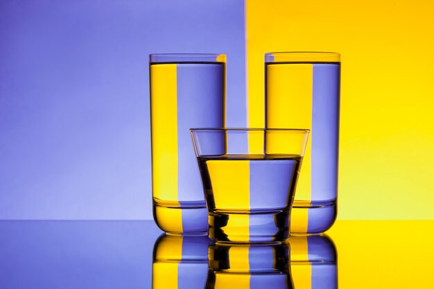 Tres vasos con agua sobre fondo morado y amarillo.