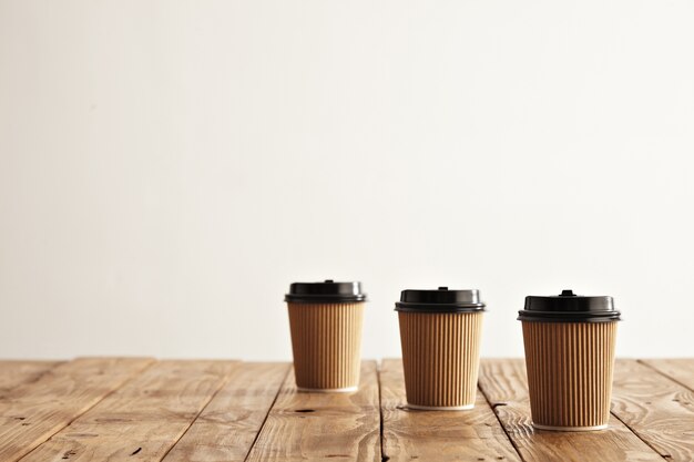 Tres vasos de cartón de papel en fila aislado en el lado derecho de la mesa de madera rústica