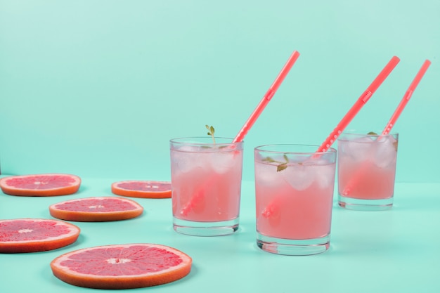 Tres vasos de jugo de pomelo frío y rodajas sobre el fondo de menta